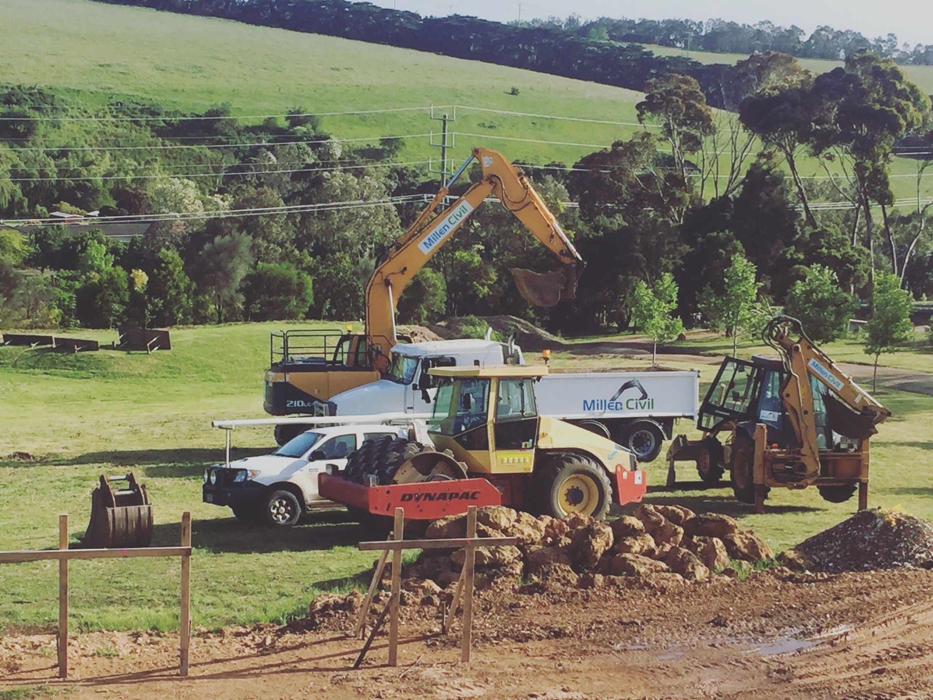 A row of construction vehicles are parked in a field
