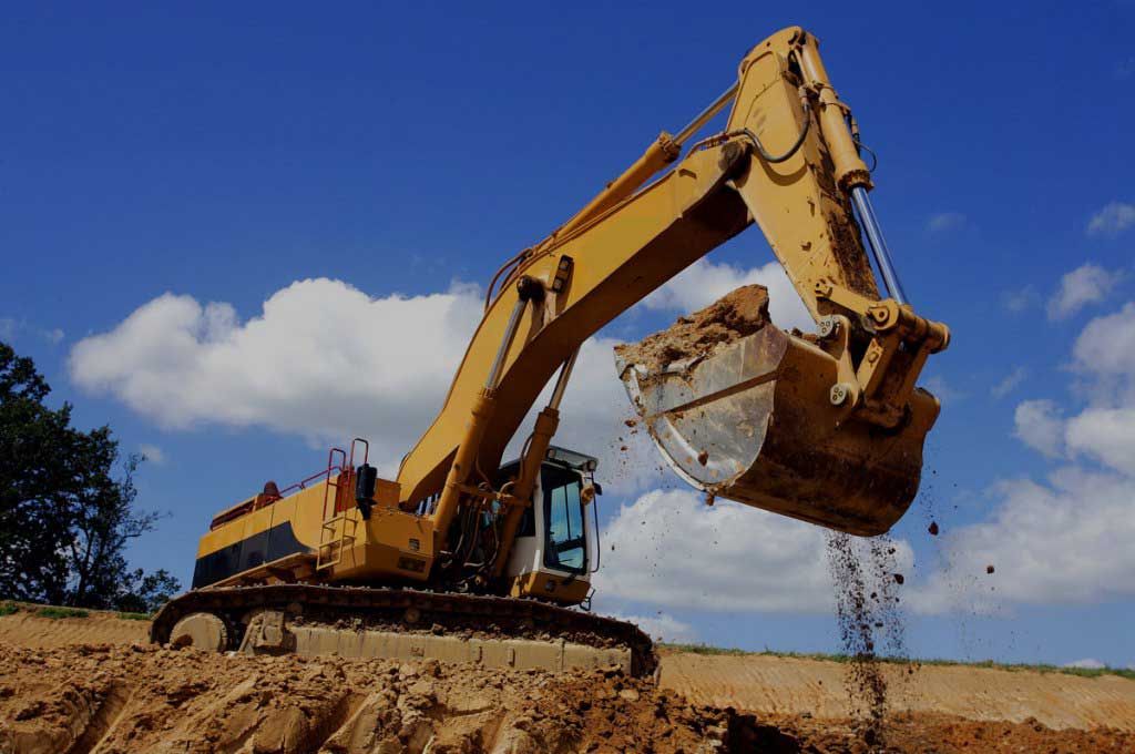 A large yellow excavator is digging a hole in a dirt field
