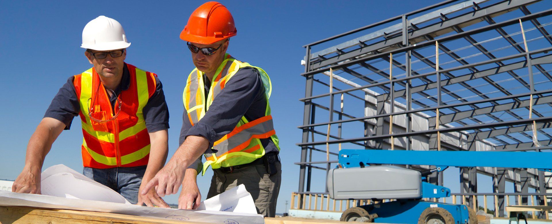 Two construction workers are looking at a blueprint at a construction site