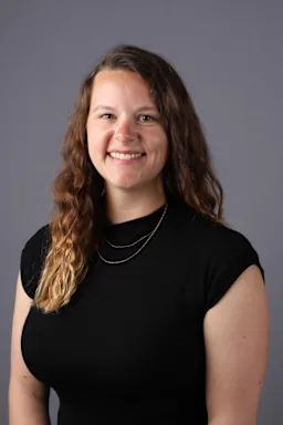 Smiling woman with long wavy brown hair, wearing a black top and a thin silver necklace.
