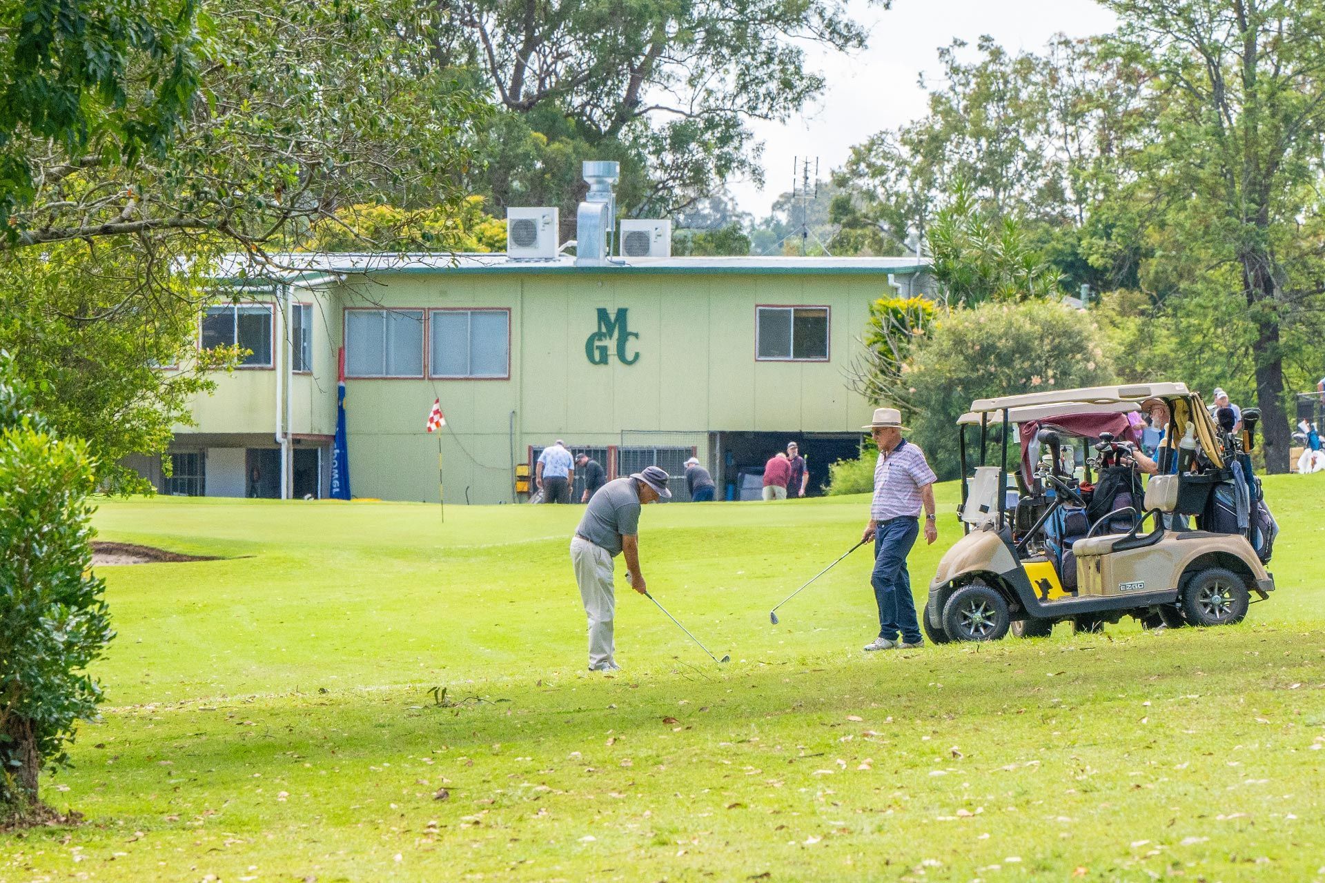 A man is swinging a golf club on a golf course next to a golf cart.