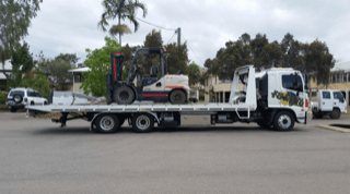 A Tow Truck Is Carrying A Forklift On The Back Of It — Day & Night Towing & Transport In Ingham, QLD