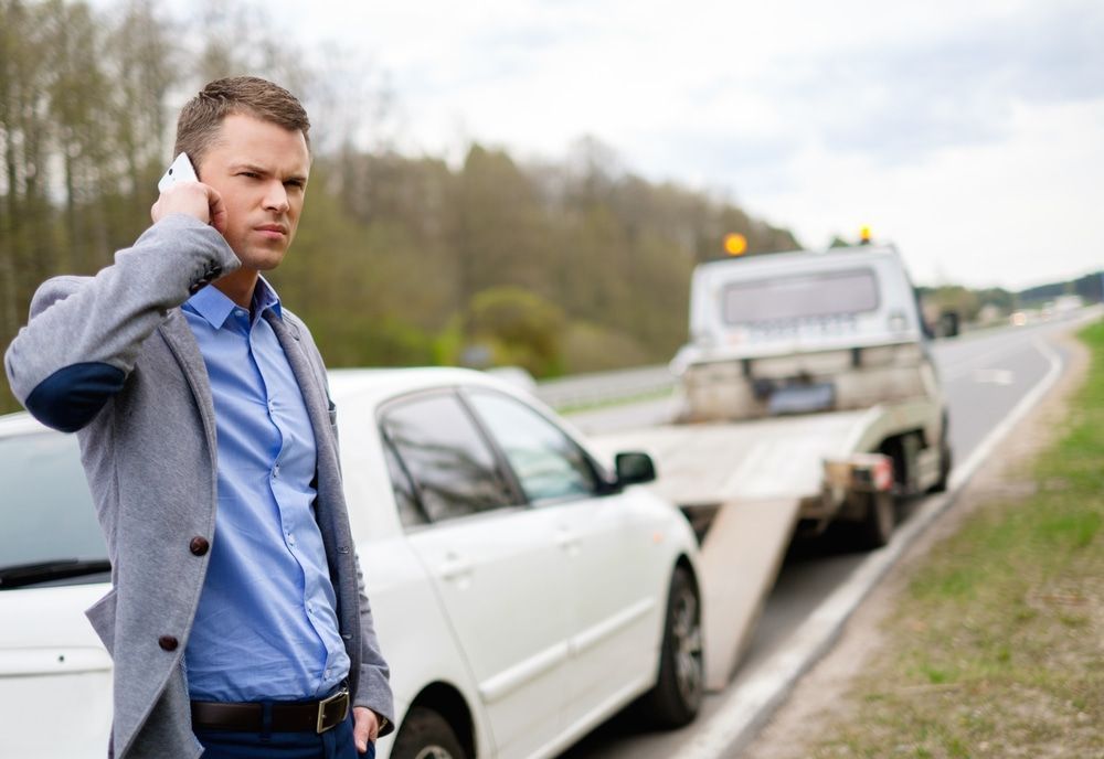 A Man Is Talking On A Cell Phone Next To A Tow Truck — Day & Night Towing & Transport In Ayr, QLD