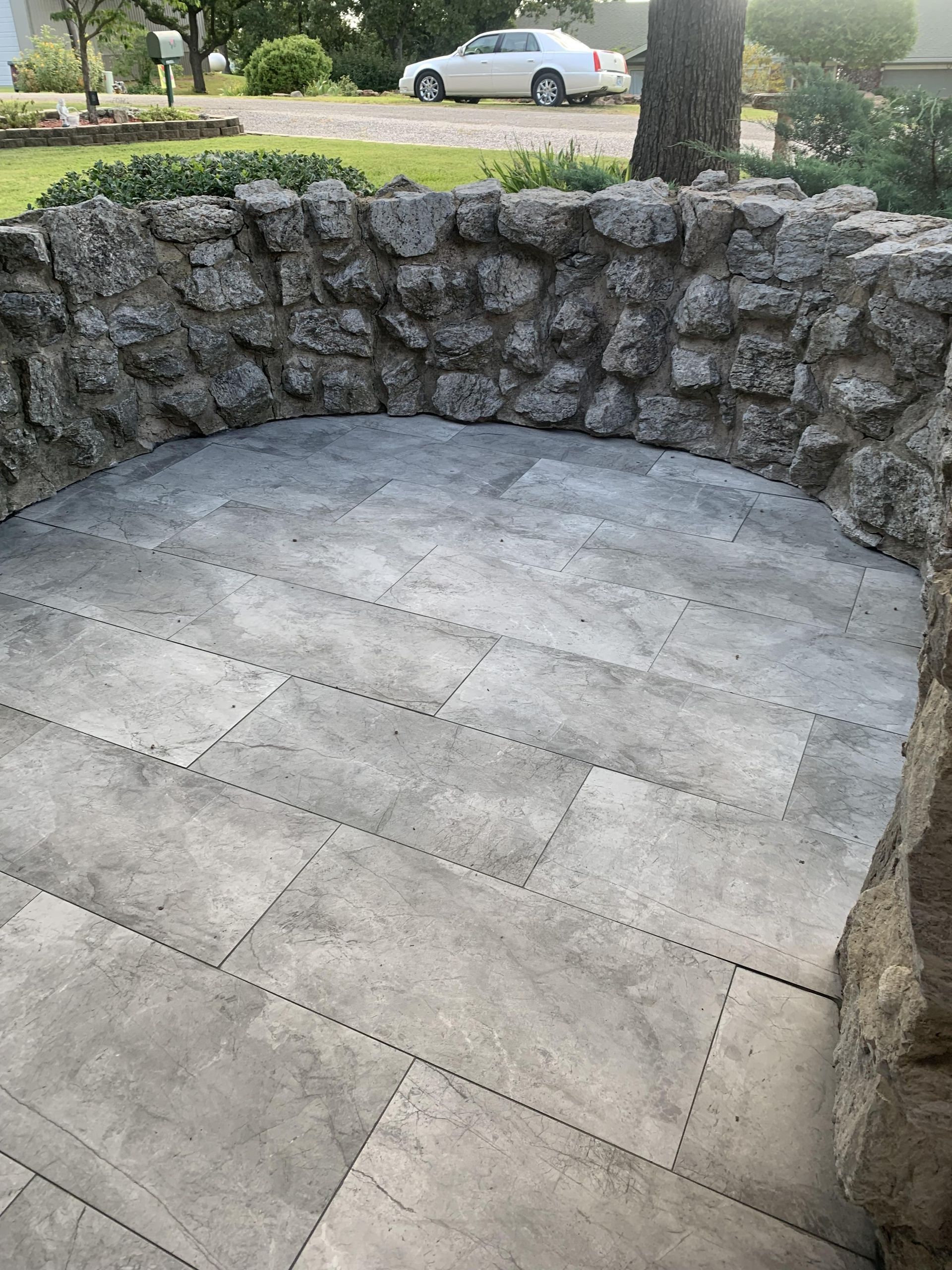 A stone wall surrounds a patio with a car parked in the background.