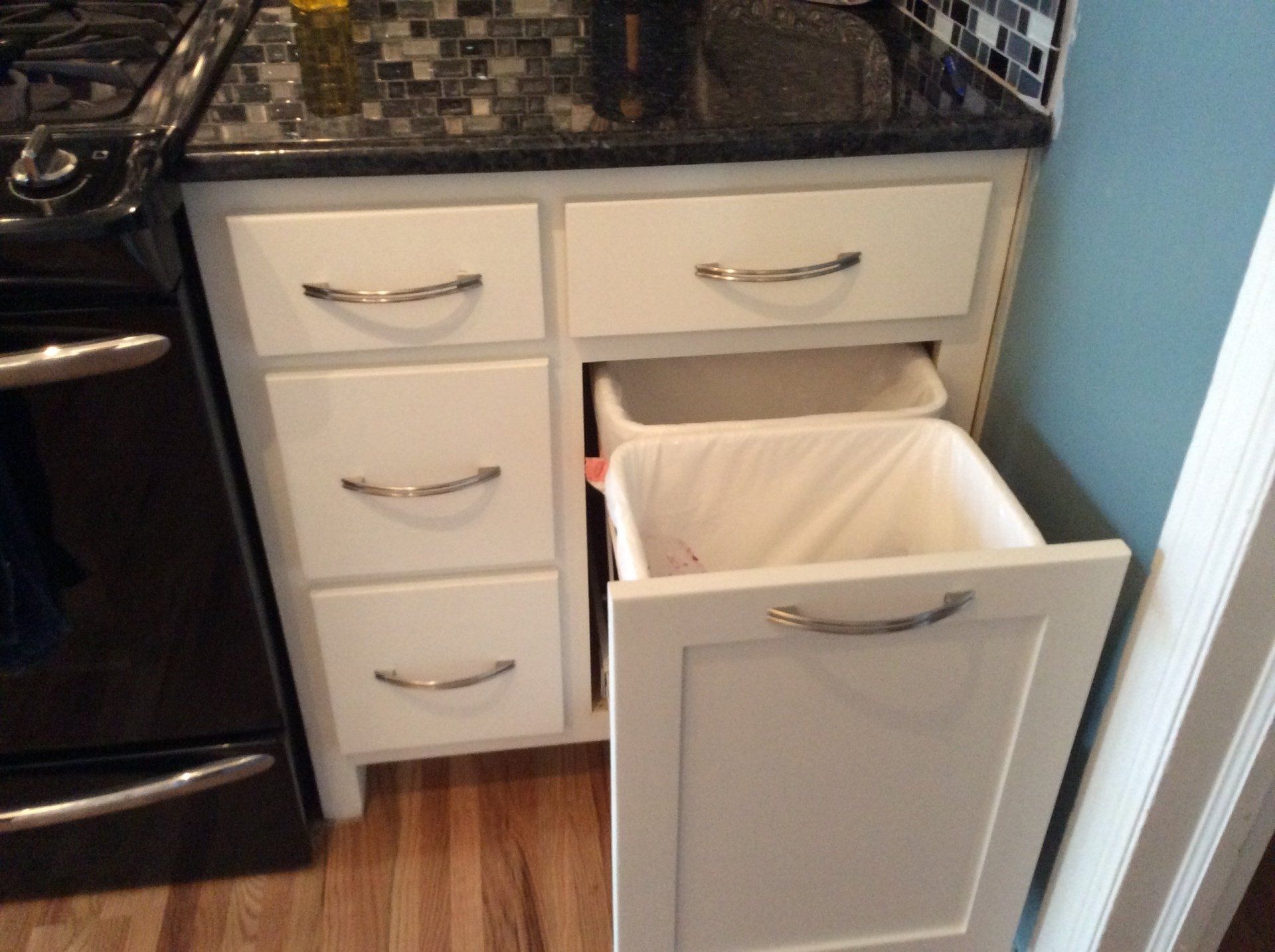 A trash can is pulled out of a cabinet in a kitchen