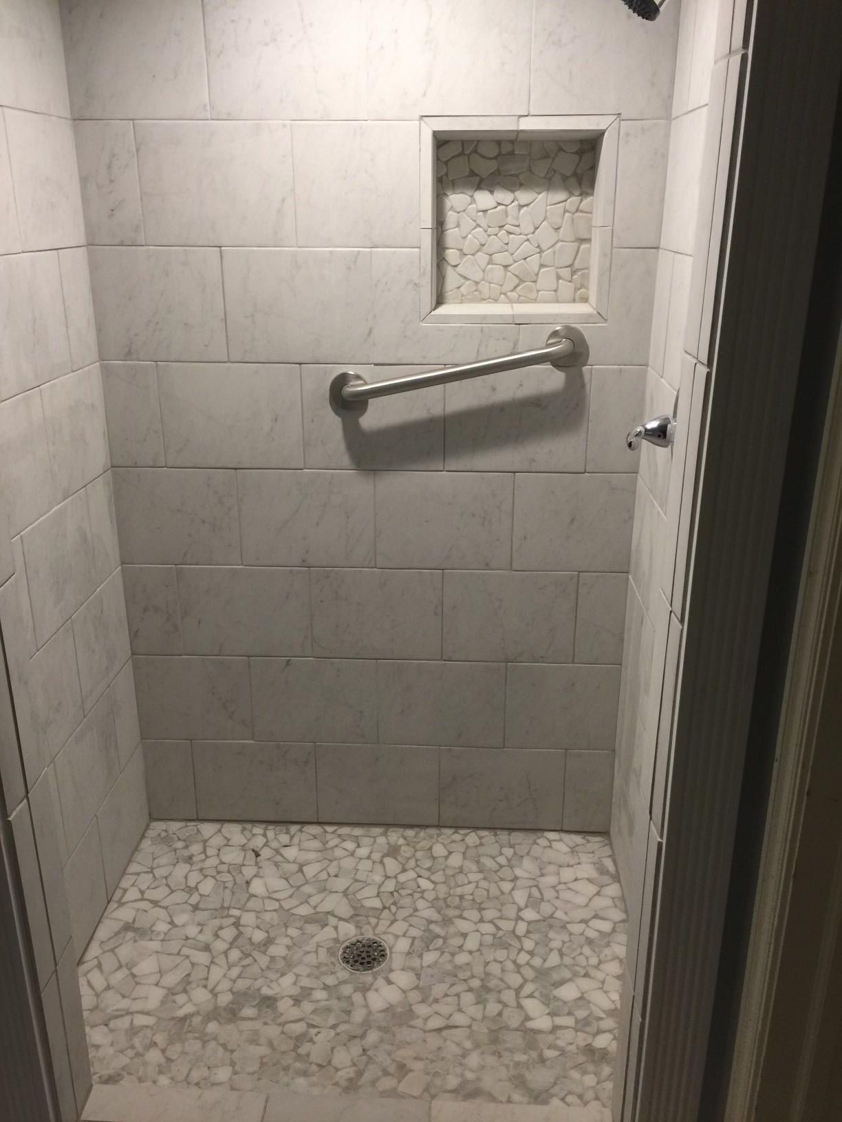 A walk in shower with white tiles and a hand rail.