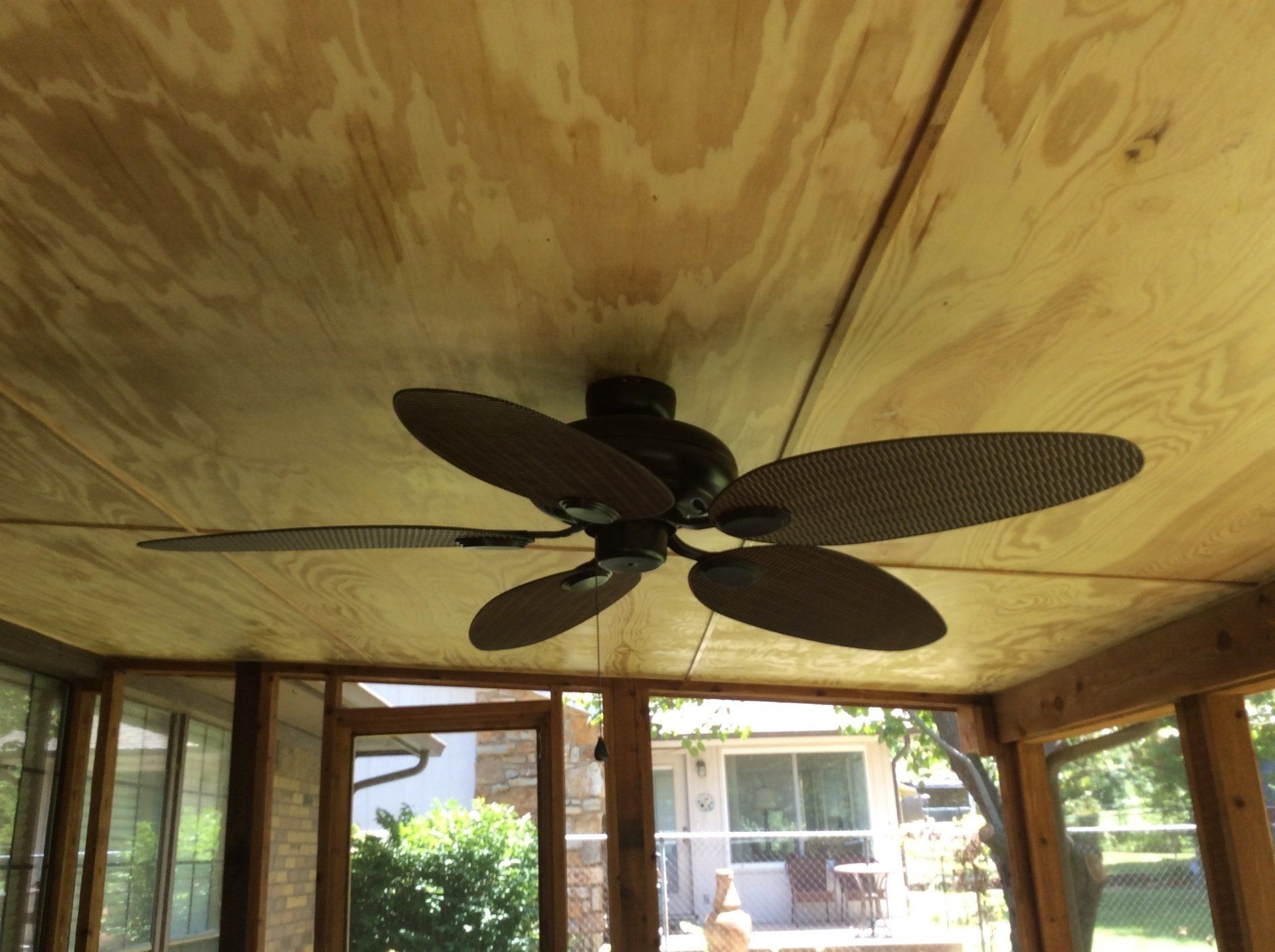 A ceiling fan is hanging from the ceiling of a screened in porch.