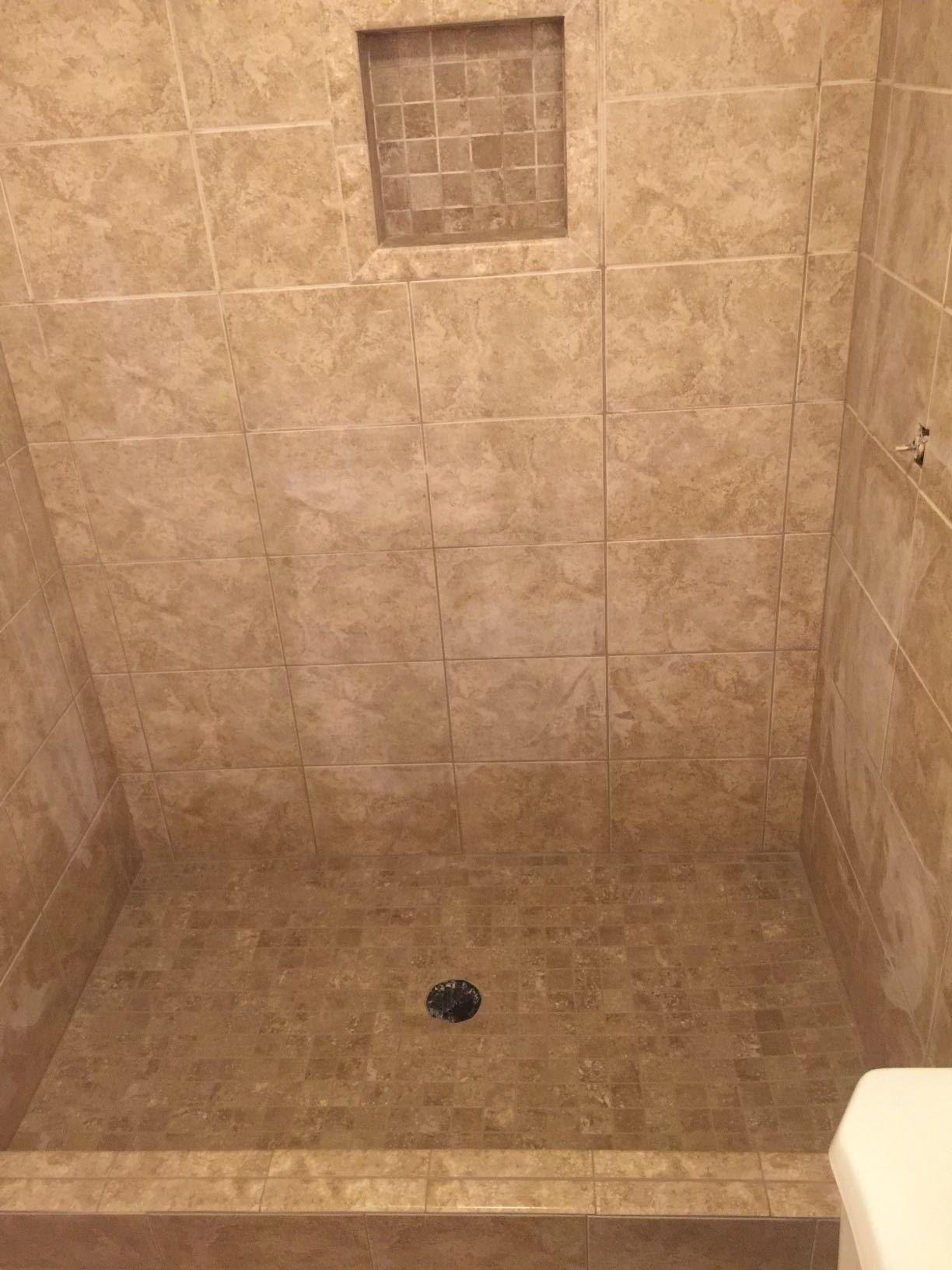 A bathroom with a tiled shower stall and a toilet.
