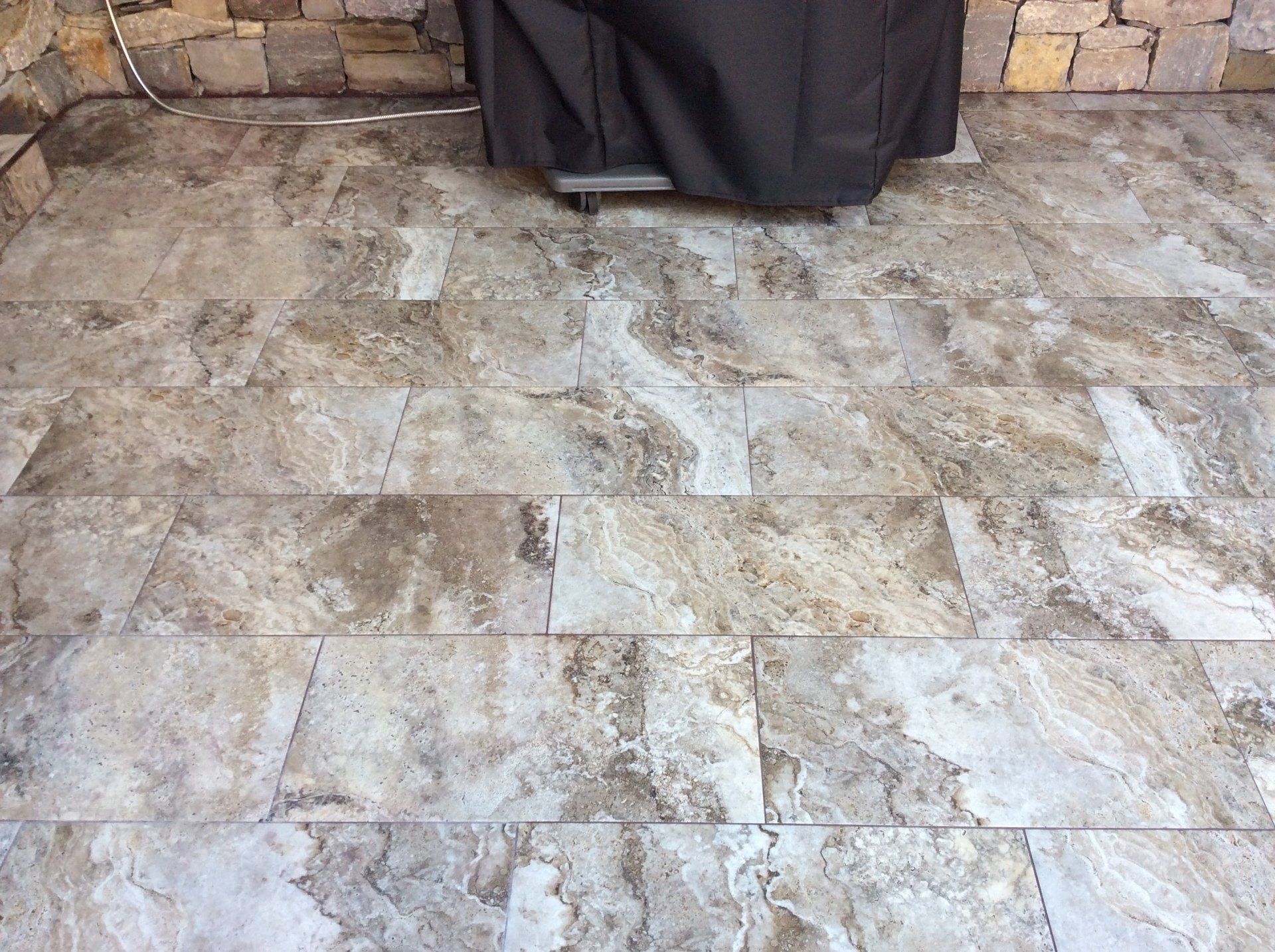 A grill is sitting on a tiled floor next to a stone wall.