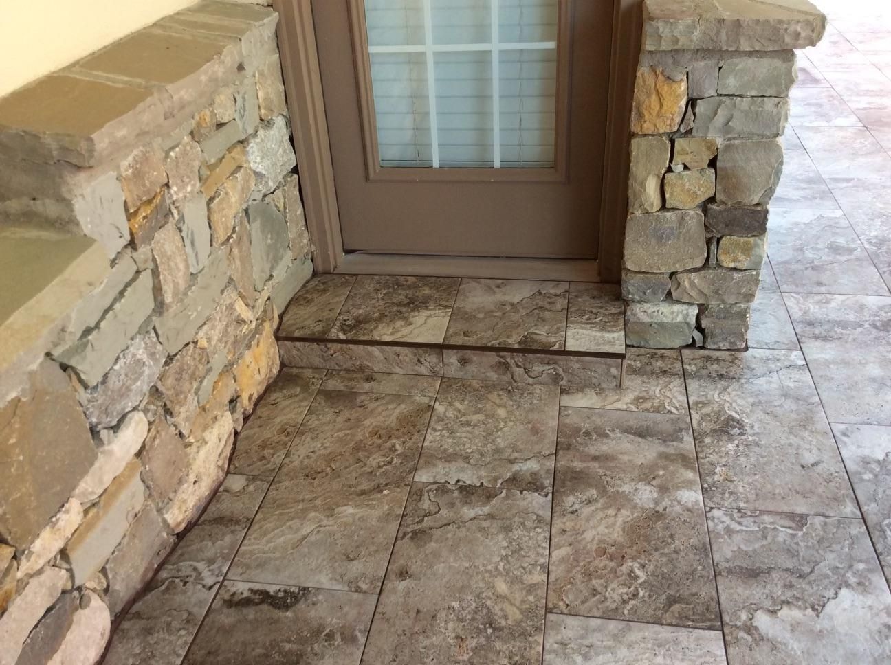 A stone wall is surrounding a tiled floor next to a door.