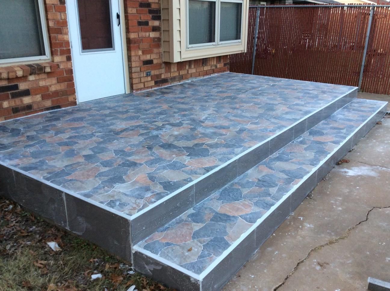 A brick house with a tiled porch and stairs in front of it.