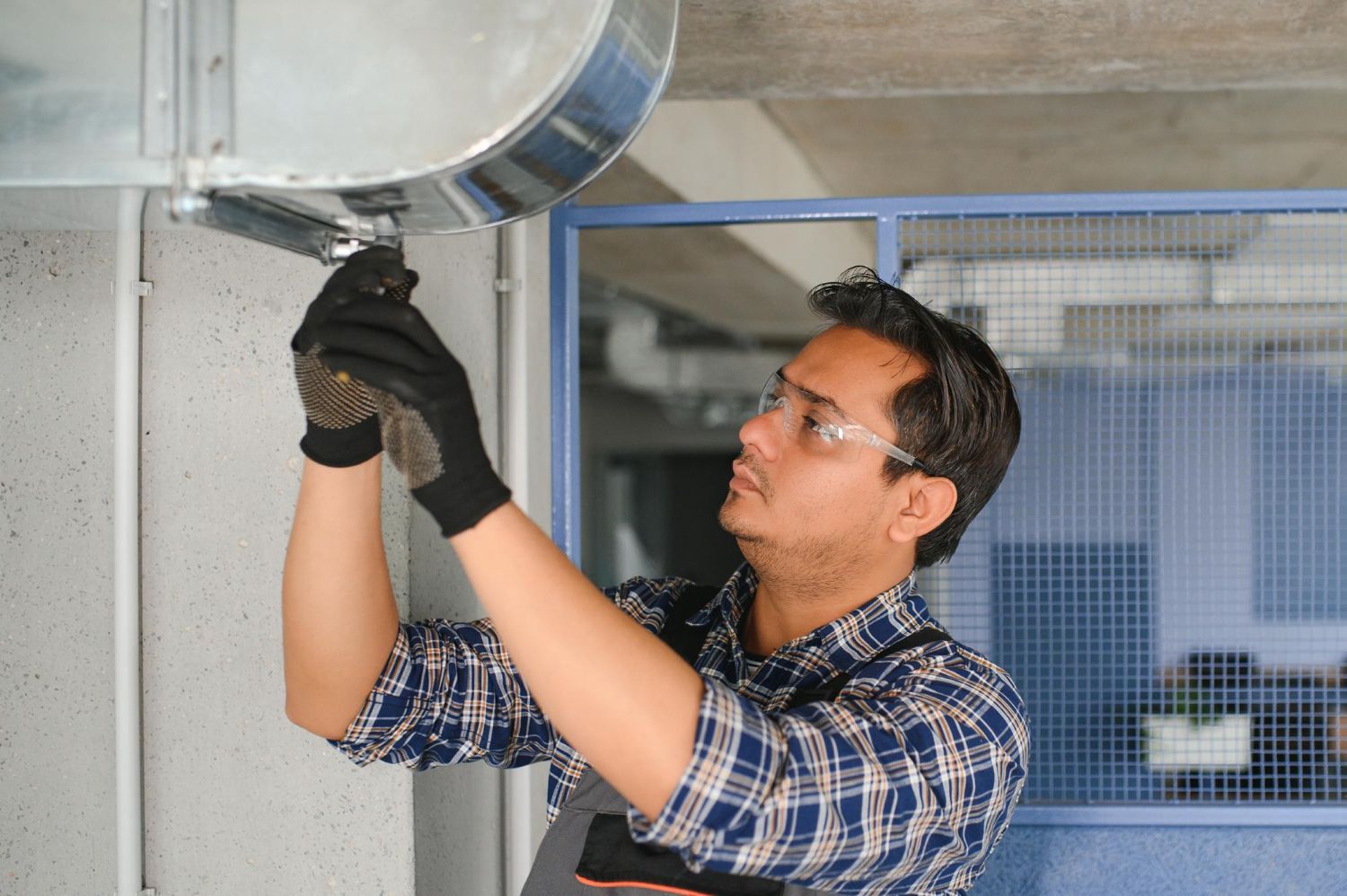 A man is working on a metal duct with a wrench.