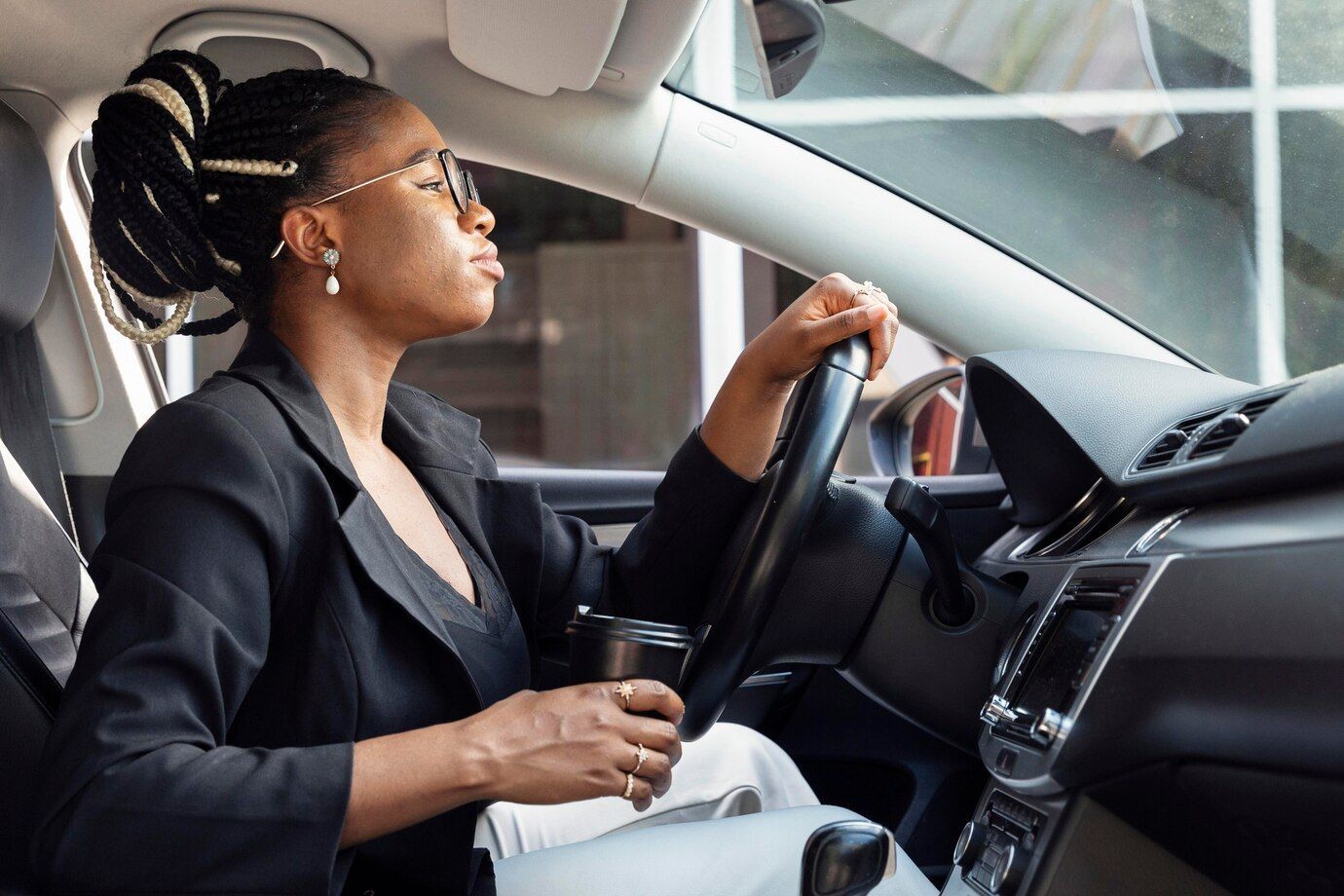 A woman is sitting in a car holding a cup of coffee.
