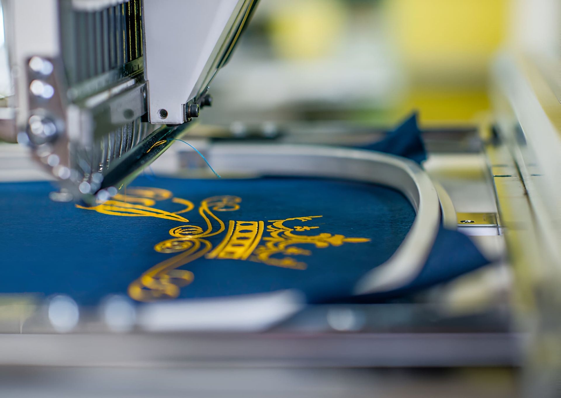 A Machine Is Embroidery A Logo On A Piece Of Blue Fabric — Gympie Embroidery Services In Southside, QLD