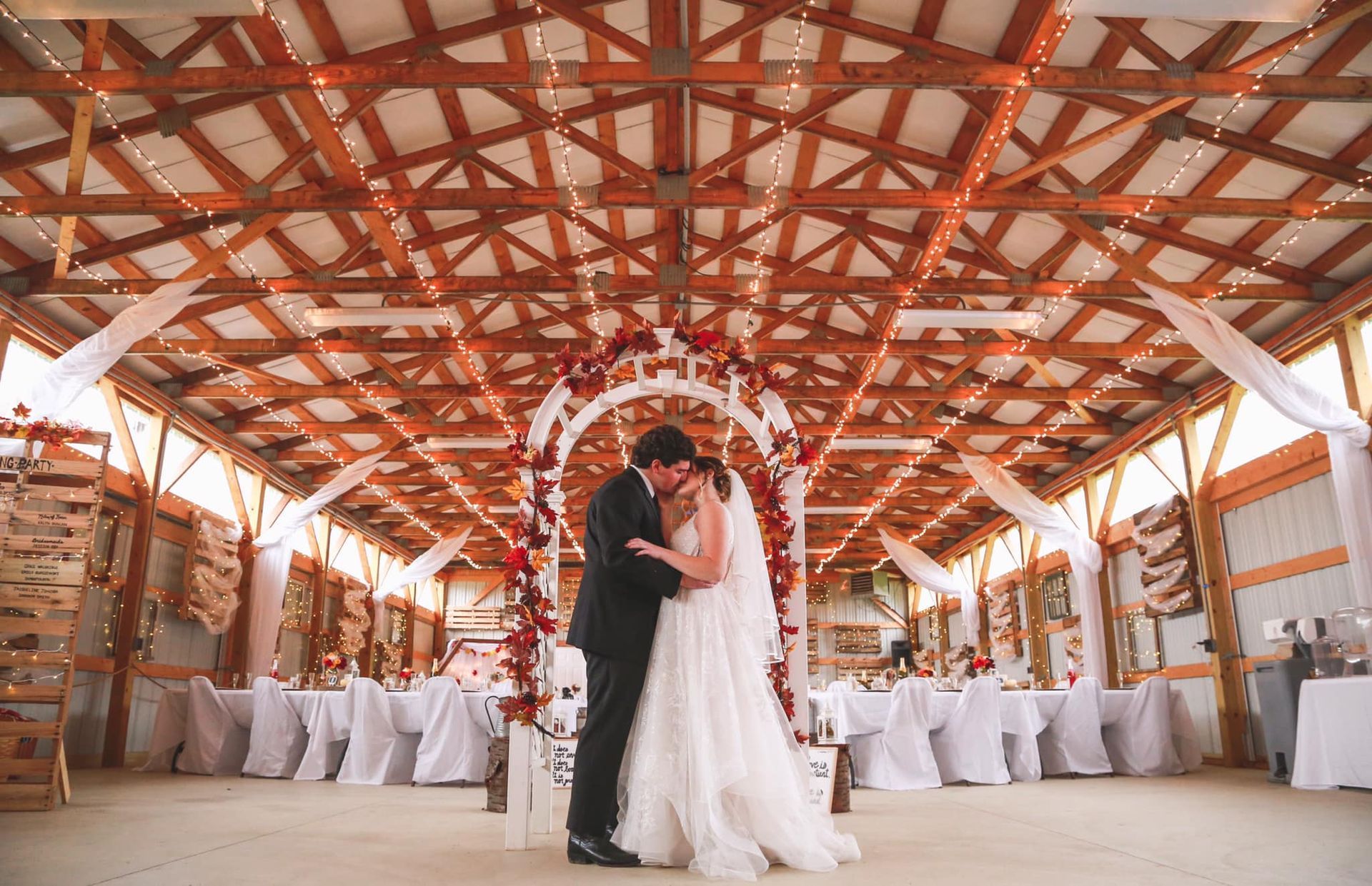 A bride and groom are kissing in a barn at their wedding reception.