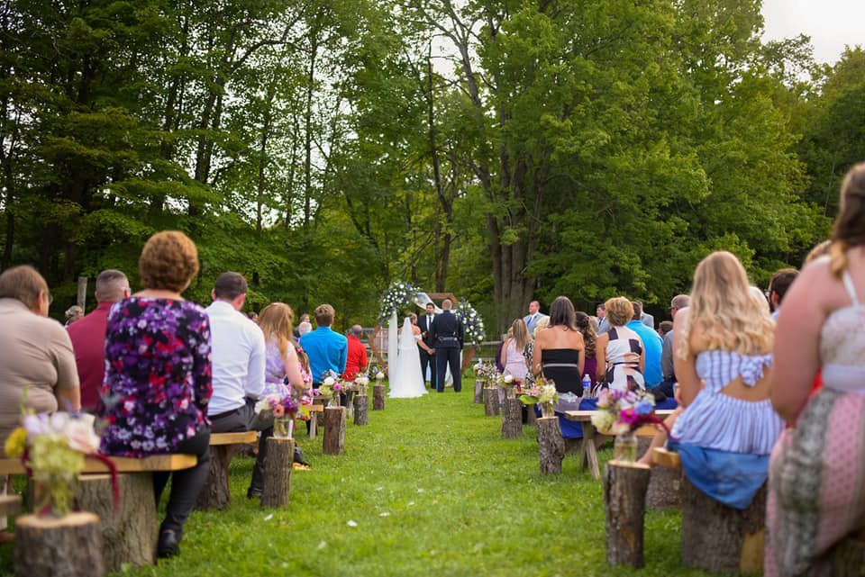 A group of people are sitting on stump benches at a wedding ceremony.