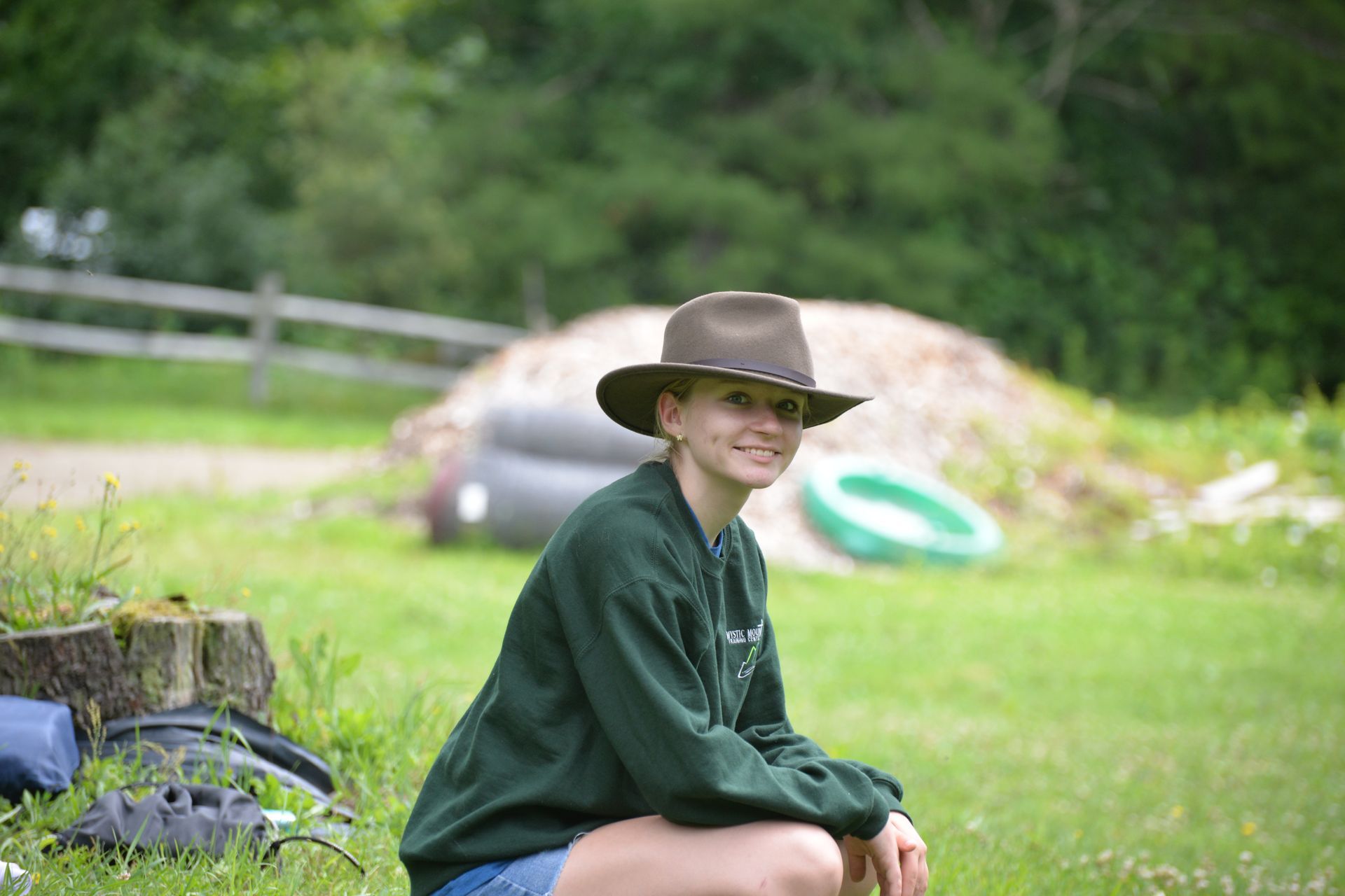 A young girl wearing a cowboy hat is sitting in the grass.