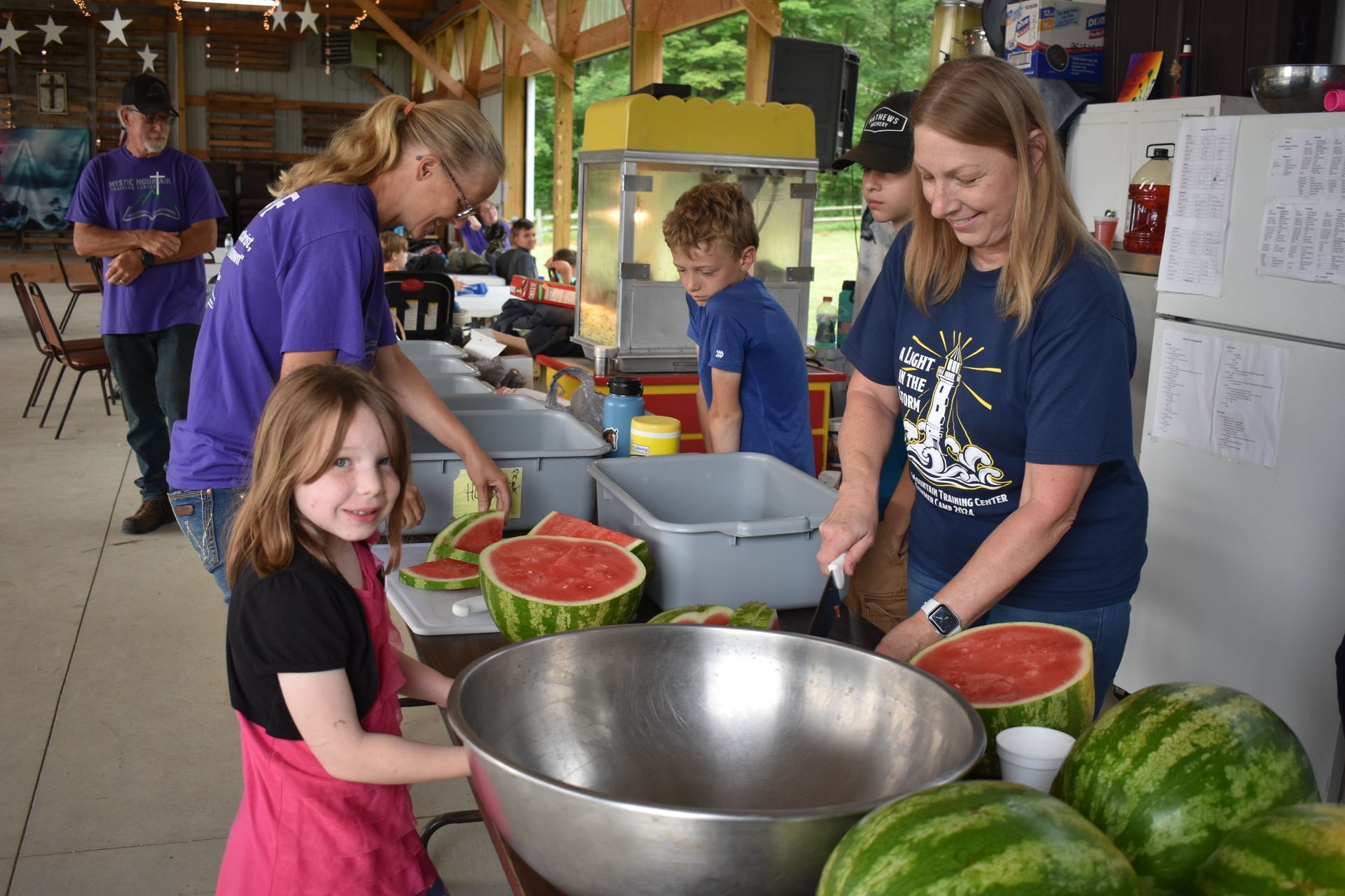 A group of people are cutting watermelons in a kitchen.