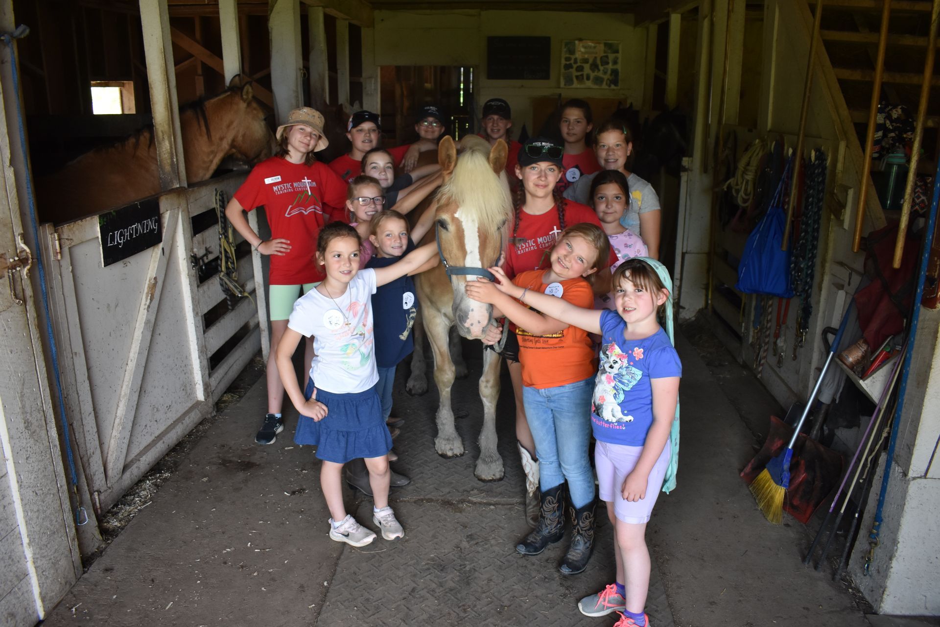 A group of children are posing for a picture with a horse in a barn.