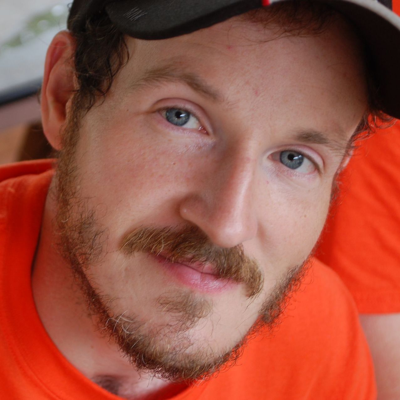 A man with a beard wearing an orange shirt and a hat
