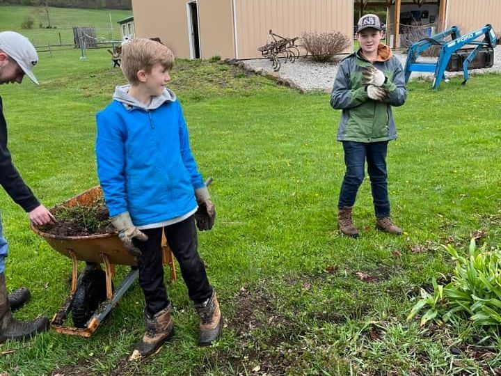 A boy is pushing a wheelbarrow full of dirt in a garden.