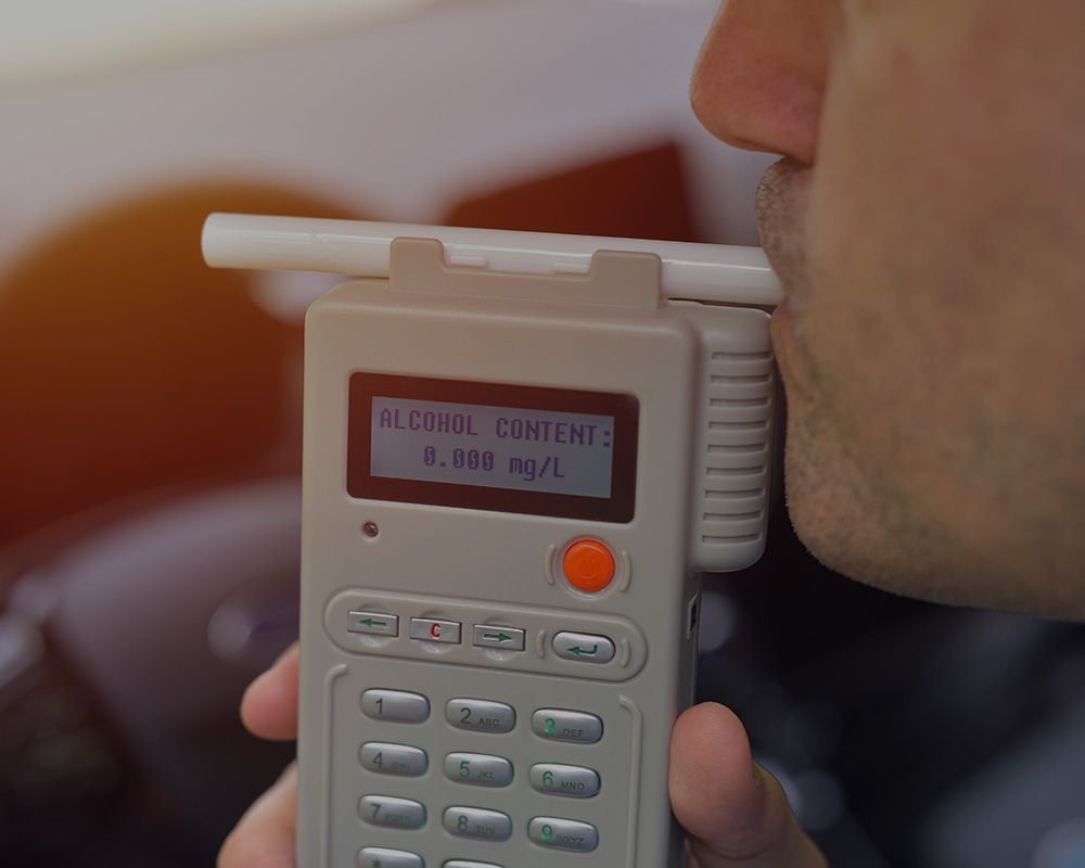 A man is taking a breathalyzer test in a car.