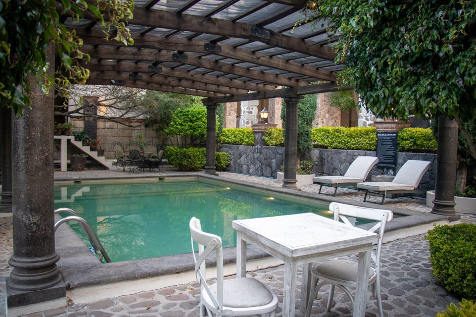Pool and patio area with a pergola, lounge chairs, and a white table and chairs.