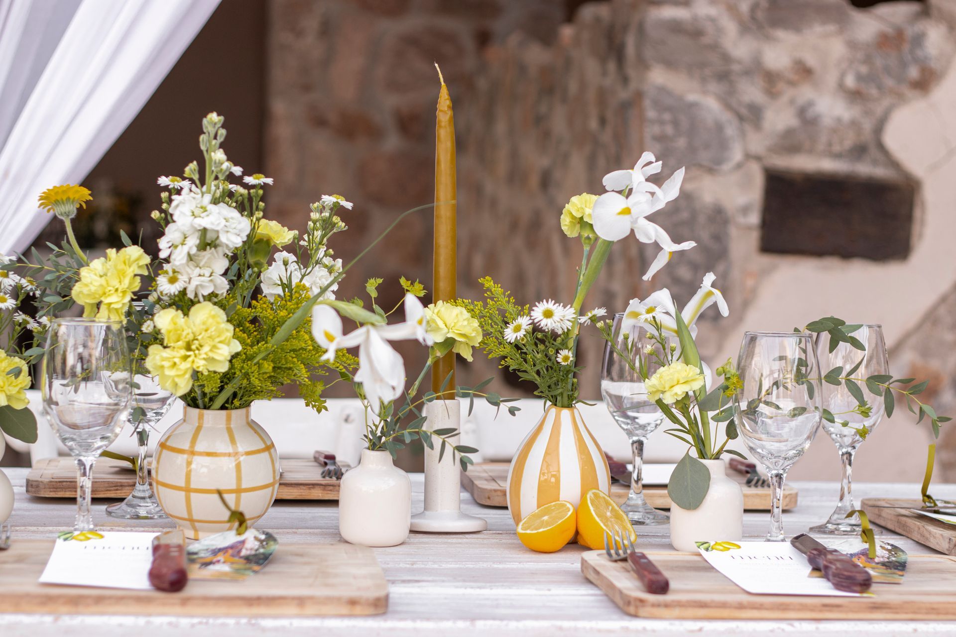Festive table setting with yellow and white flowers, candles, and glassware.