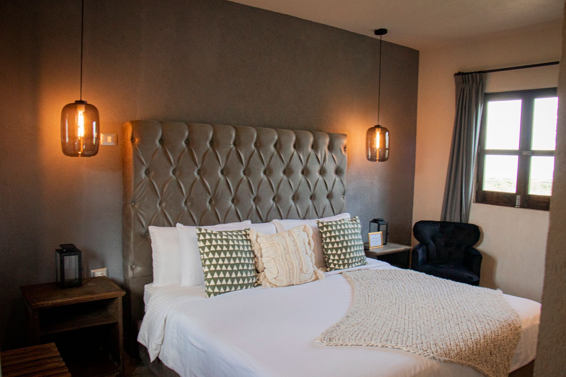 Bedroom with a large bed, tufted headboard, and pendant lights, near a window.