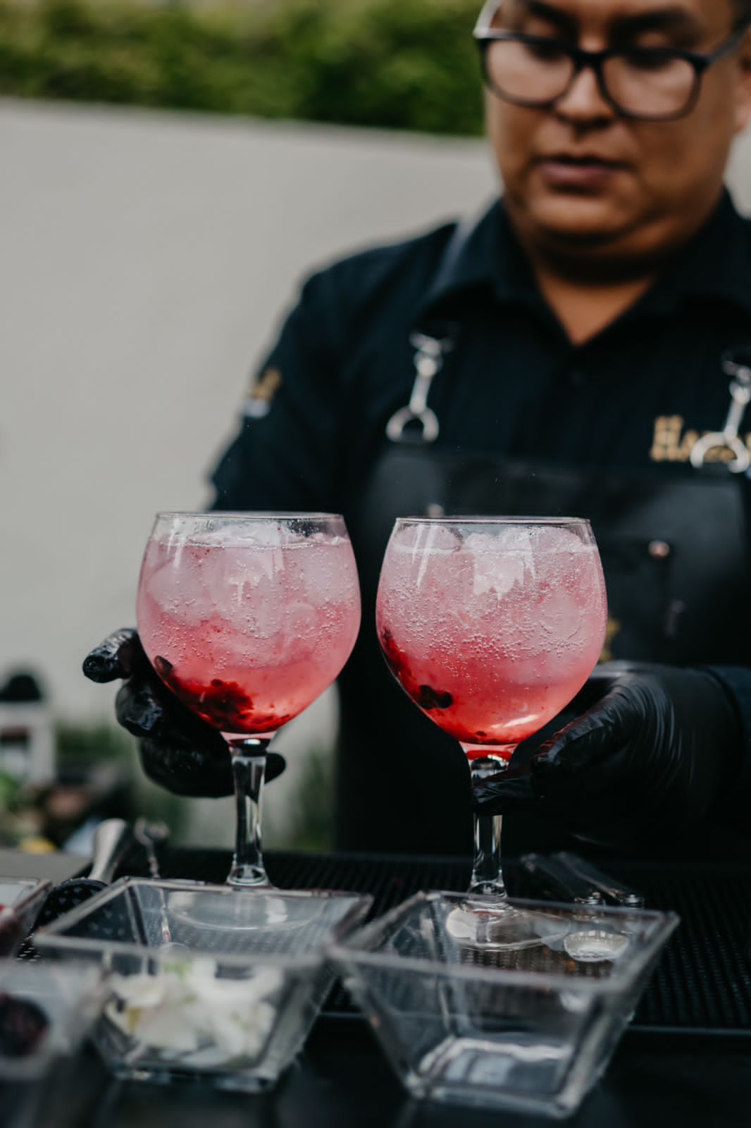 Bartender holding two pink cocktails in stemmed glasses.