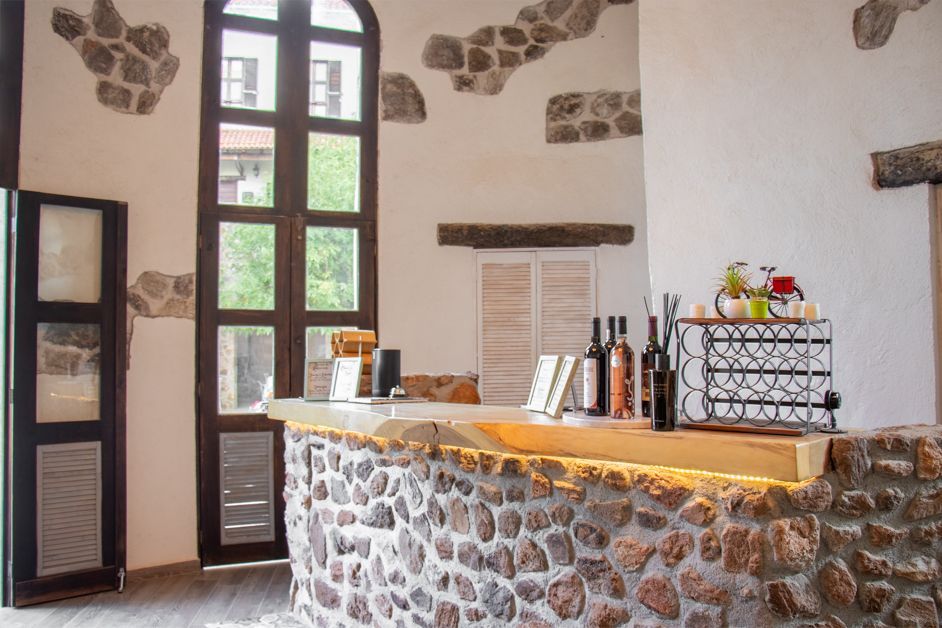 Stone-covered bar counter in a rustic room. Tall window and white walls with stone accents. Bottles and decor on the counter.