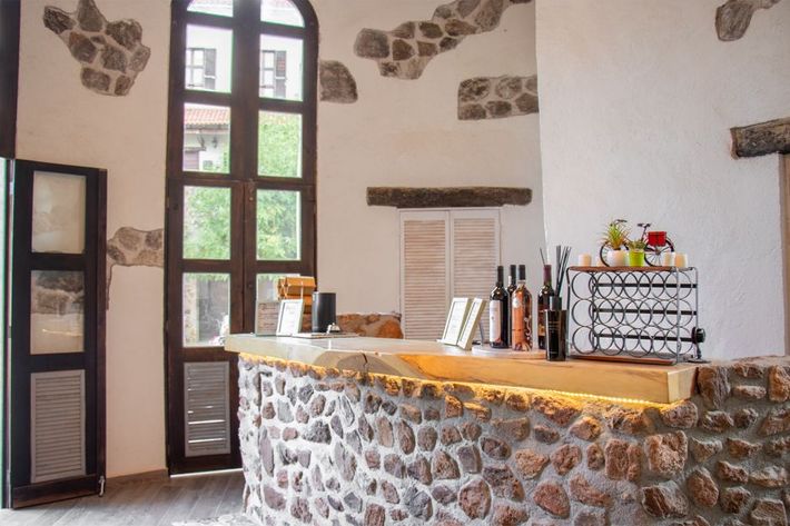 Bar with stone facade, tall window, bottles, white walls, and a wooden counter.