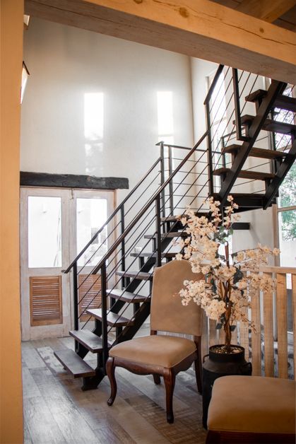 Interior view: Staircase with black metal railings, light wood floors, and a vintage chair.