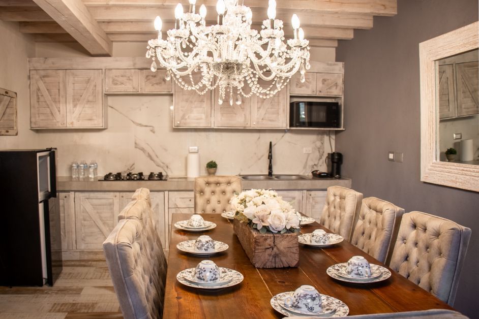 Kitchen and dining area with chandelier, wooden cabinets, and a long table set for dinner.