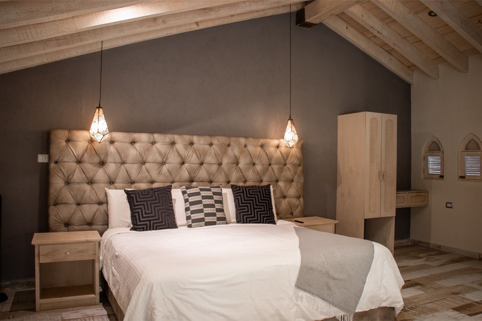 Bedroom with large tufted headboard, bed, nightstands, and wardrobe. Gray wall, pendants, wood ceiling.