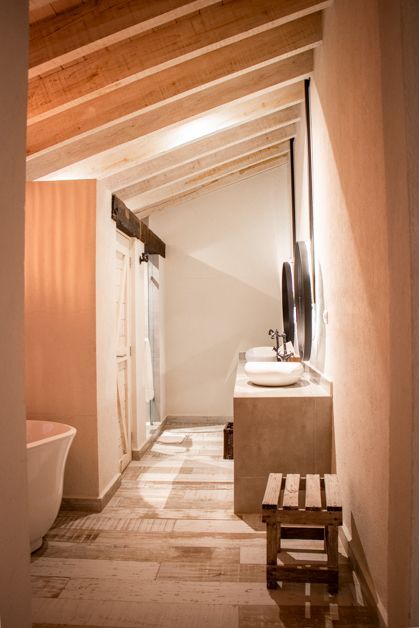 Bathroom with sloped ceiling, wooden beams, light wood floors, stone vanity, tub.