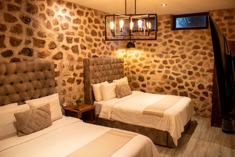 Two beds in a room with stone walls, a light fixture, and a small window.