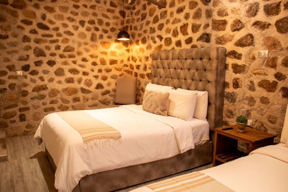 Bedroom with stone walls, two beds, a cushioned headboard, and warm lighting.