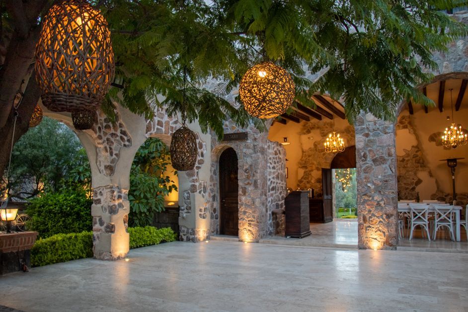 Stone arched patio with hanging lanterns, a tree, and a glimpse of a restaurant interior.