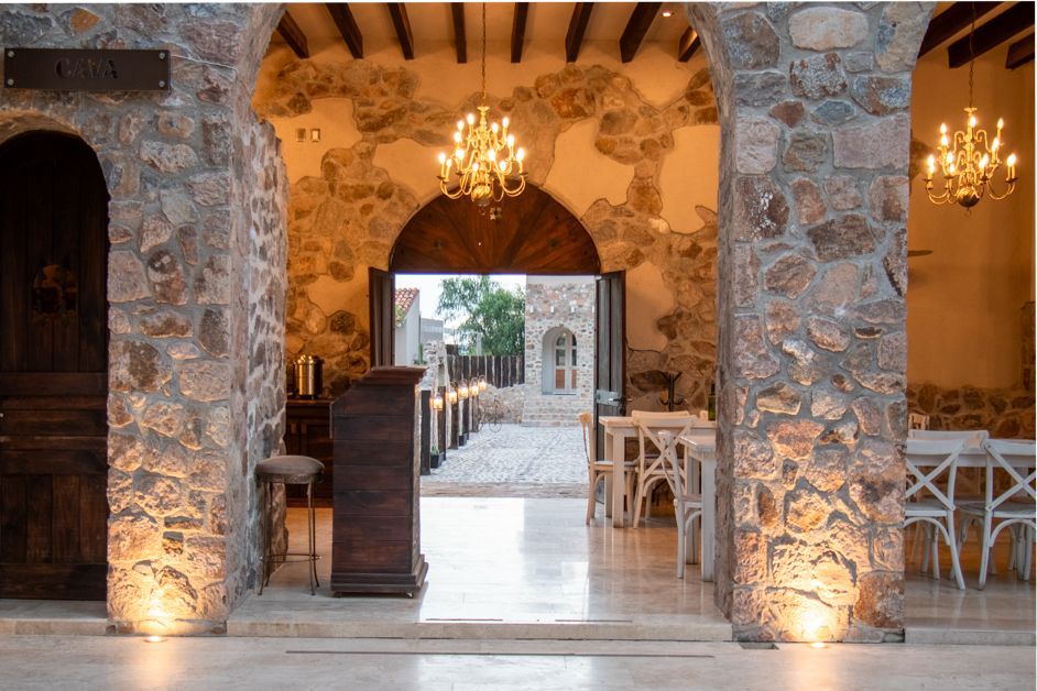 Stone arched doorway leading to a courtyard with tables and chairs, lit by chandeliers.