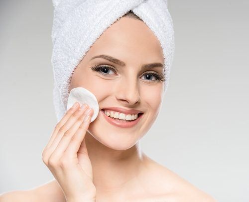 Una mujer con una toalla envuelta alrededor de su cabeza se limpia la cara con un algodón.