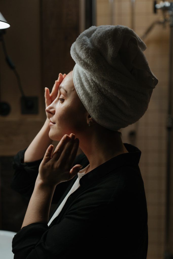 una mujer con una toalla envuelta alrededor de su cabeza se mira la cara en el espejo.