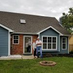 A couple of people are standing in front of a house.