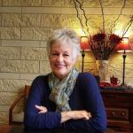 A woman is sitting at a table with her arms crossed and smiling.