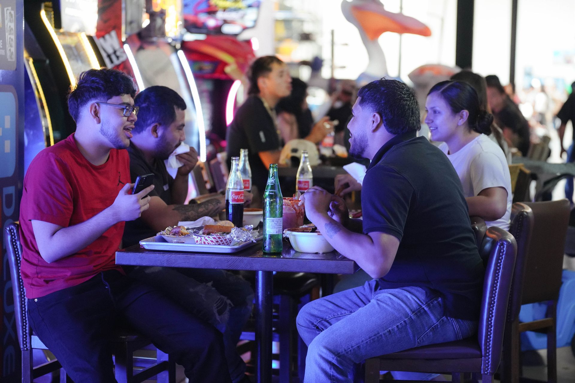 People eating and talking at a table in a restaurant with arcade games in the background.