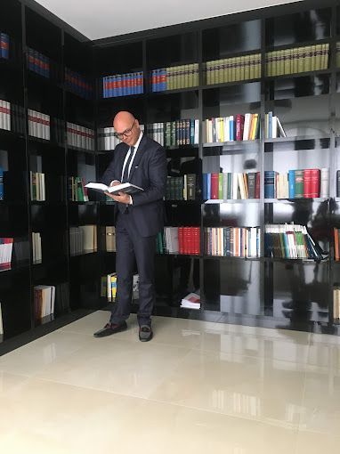 Un uomo in giacca e cravatta sta leggendo un libro in una biblioteca.