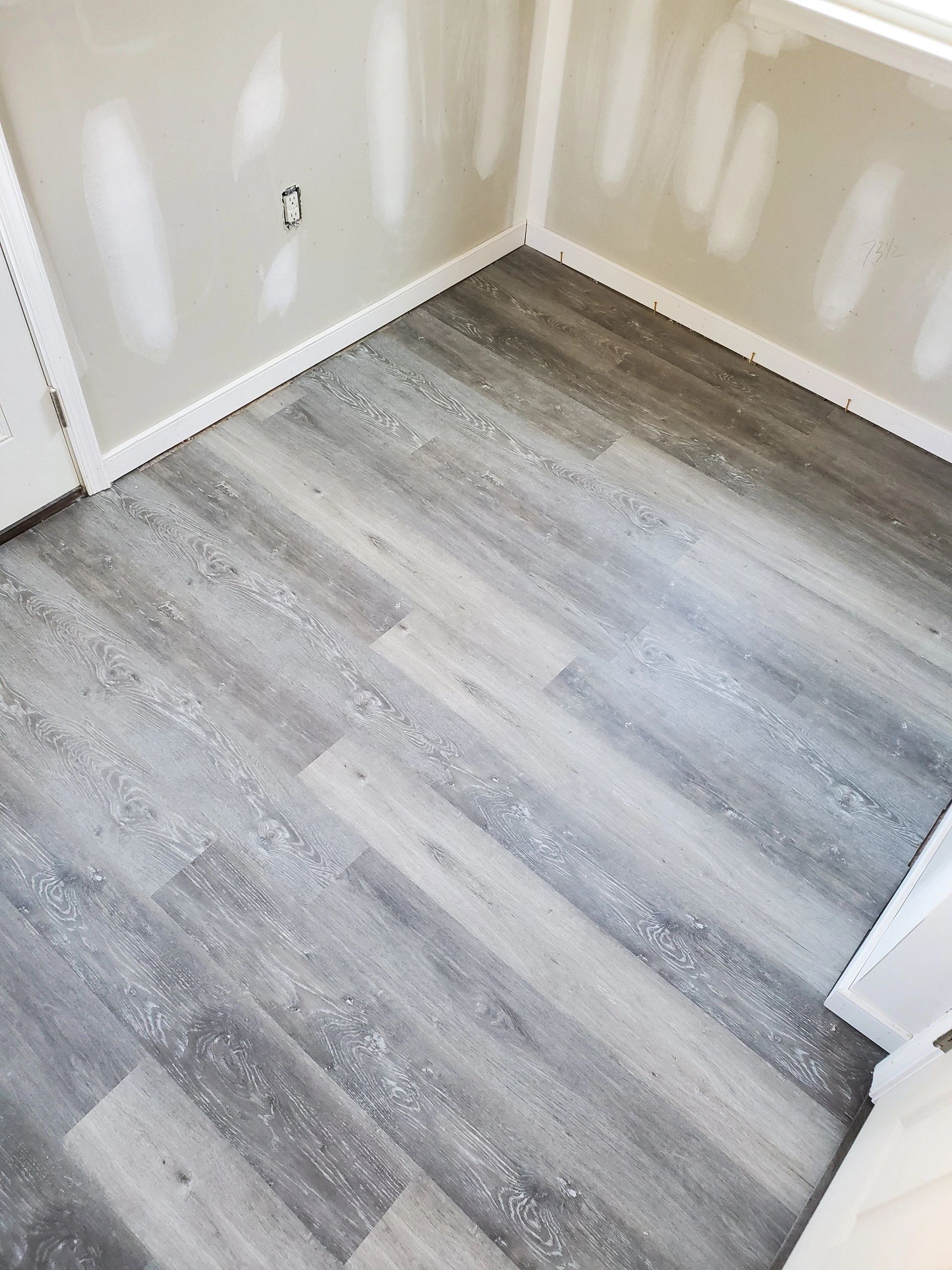 Gray vinyl plank flooring in a room with unfinished drywall and white trim.