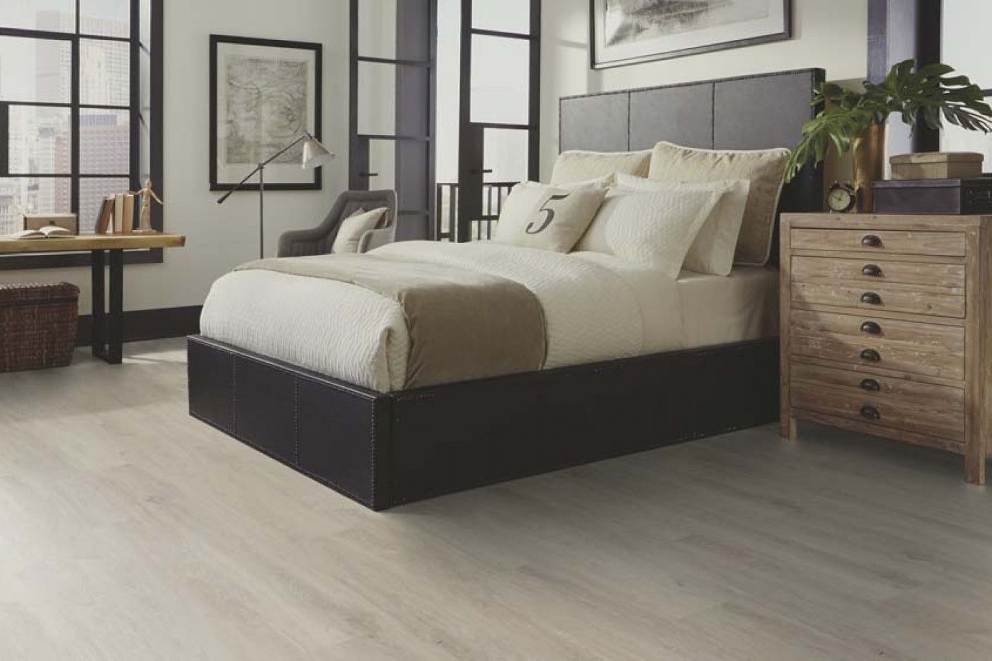 Bedroom with a dark bed frame, neutral bedding, wood dresser, large windows, and light wood-look floor.