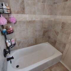 A bathroom with a white bathtub, tan tiled walls, and a black shower caddy with bath products.