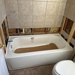 A bathtub is being installed in a bathroom. The surrounding walls are unfinished with exposed studs and tiles.
